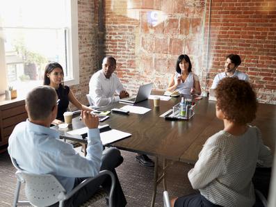 A group of six people around a large table having a business meeting